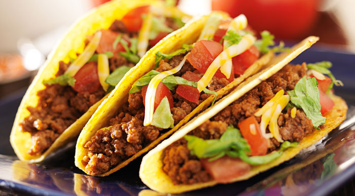 Latin American food three beef tacos with cheese, lettuce and tomatoes